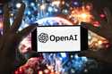 The OpenAI logo is displayed on a cell phone in front of an image generated by ChatGPT's Dall-E tex…