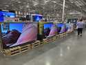 A shopper passes by a display of large-screen televisions in a Costco warehouse Monday, February 3,…