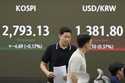 Currency traders walk by the screen showing the Korea Composite Stock Price Index…