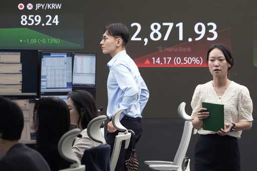 A currency trader passes by the screen showing the Korea Composite Stock Price Index…