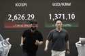 Currency traders pass by a screen showing the Korea Composite Stock Price Index…