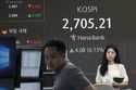 Currency traders work near a screen showing the Korea Composite Stock Price Index…