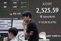 A currency trader walks by the screens showing the Korea Composite Stock Price Index…