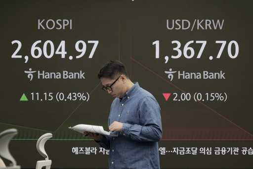 A currency trader reads documents near a screen showing the Korea Composite Stock Price Index…