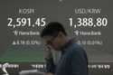 A currency trader walks by the screens showing the Korea Composite Stock Price Index…