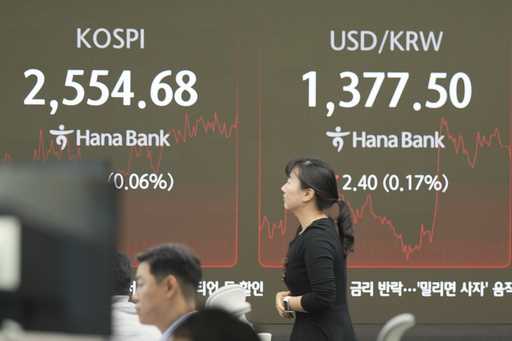 A currency trader walks by the screen showing the Korea Composite Stock Price Index…