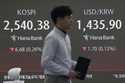 A currency trader passes by a screen showing the Korea Composite Stock Price Index…