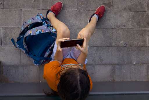 A 11-year-old boy plays with his father's phone outside school in Barcelona, Spain, Monday, June 17…