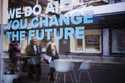 People reflected in a window with a slogan about AI at a representation of a company ahead of the W…