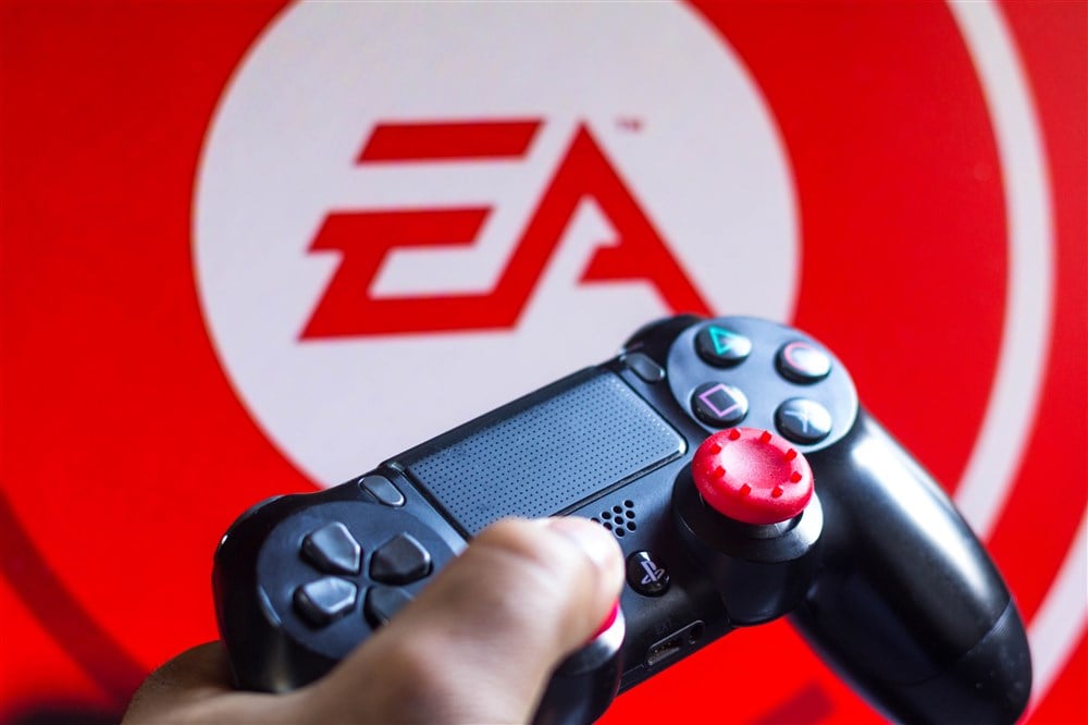 ea logo on red and white background with gaming controller and thumb in foreground
