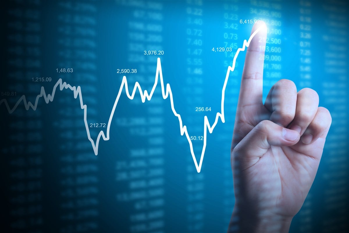 illustration of a hand with finger drawing a stock price chart on technical background