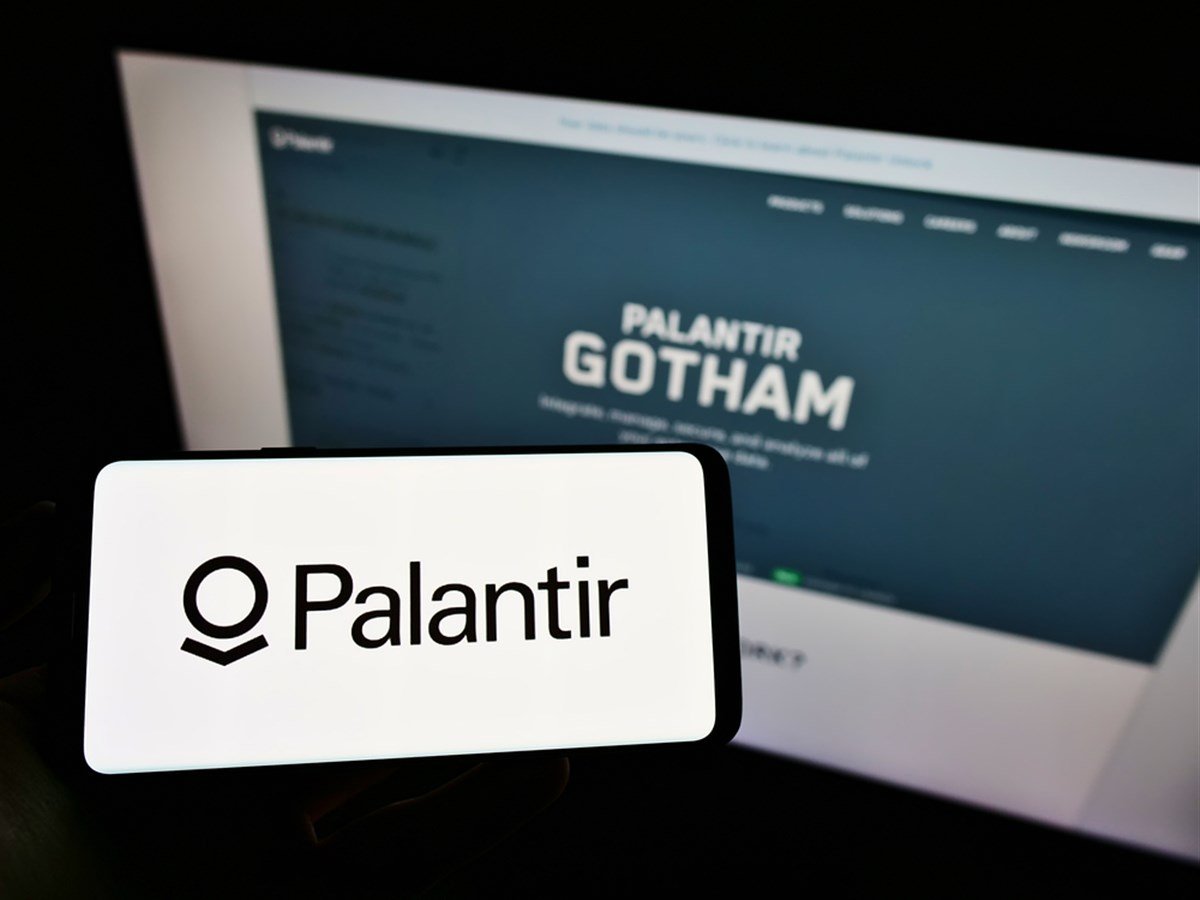 Person holding mobile phone with logo of American software company Palantir Technologies Inc. on screen in front of web page