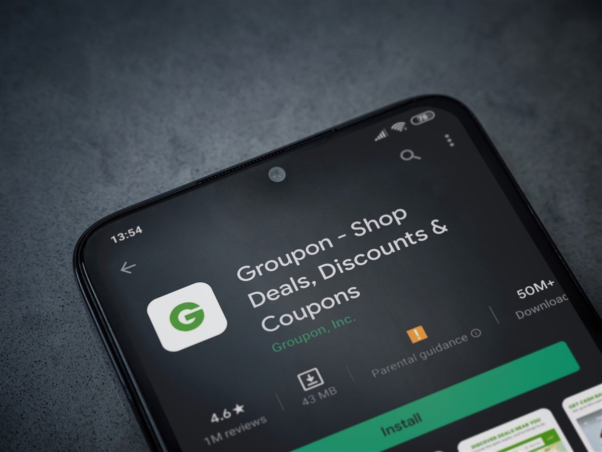 Groupon app play store page on the display of a black mobile smartphone on dark marble stone background