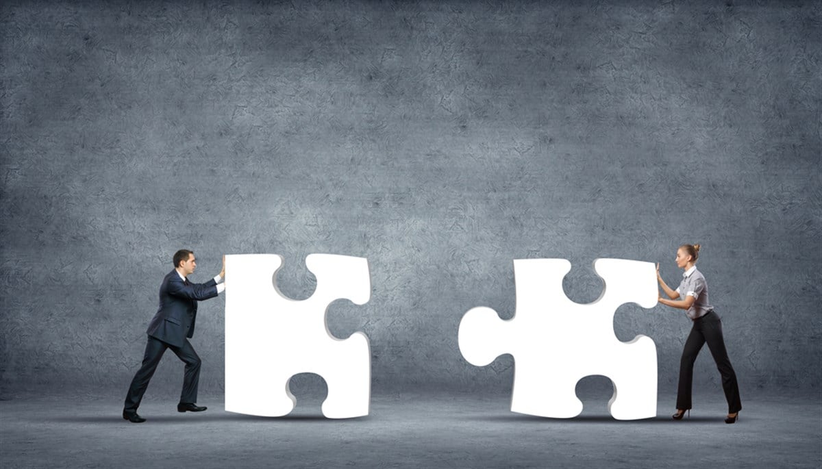 Photo of two business people pushing puzzle pieces together, symbolizing how two companies depend on each other 