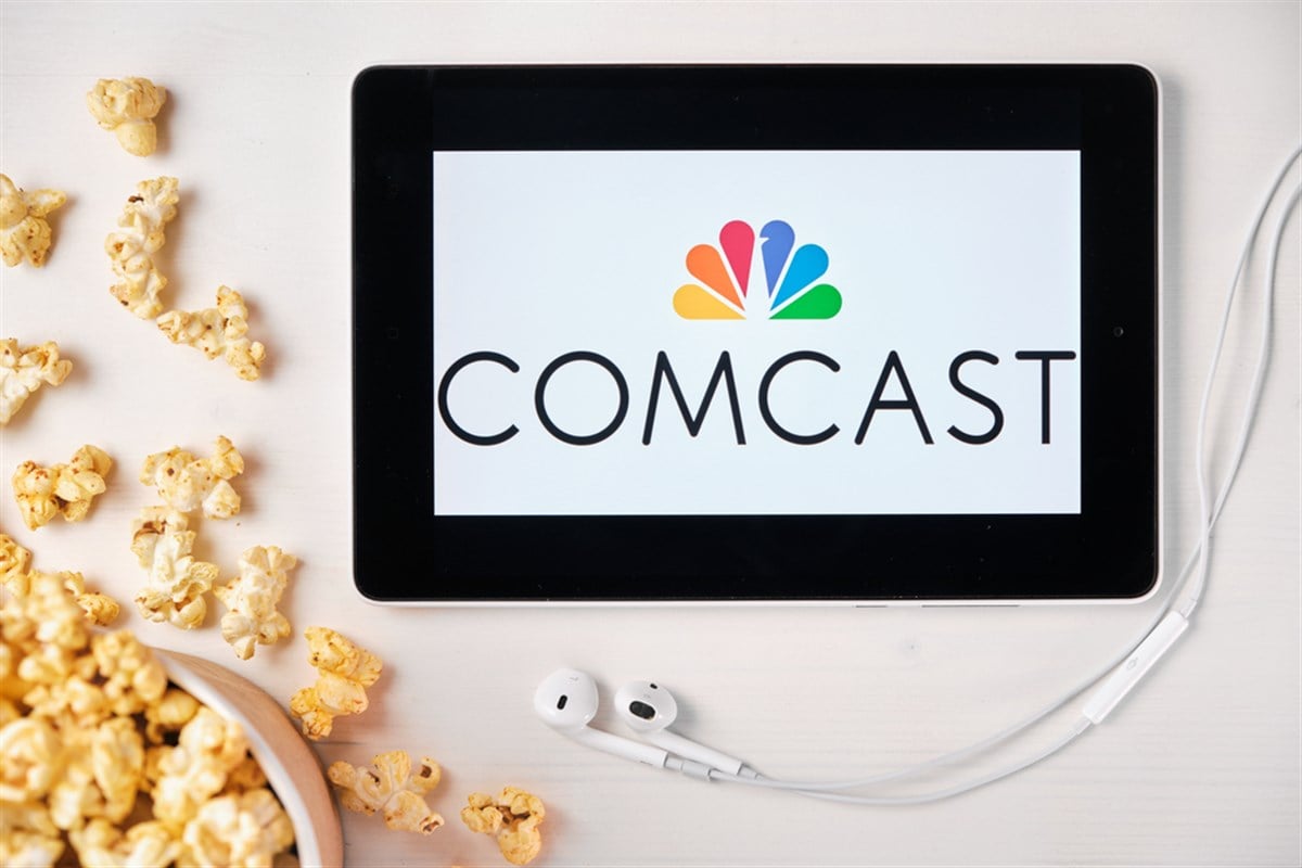 Comcast logo on the mobile phone screen with popcorn box and Apple earpods on the background