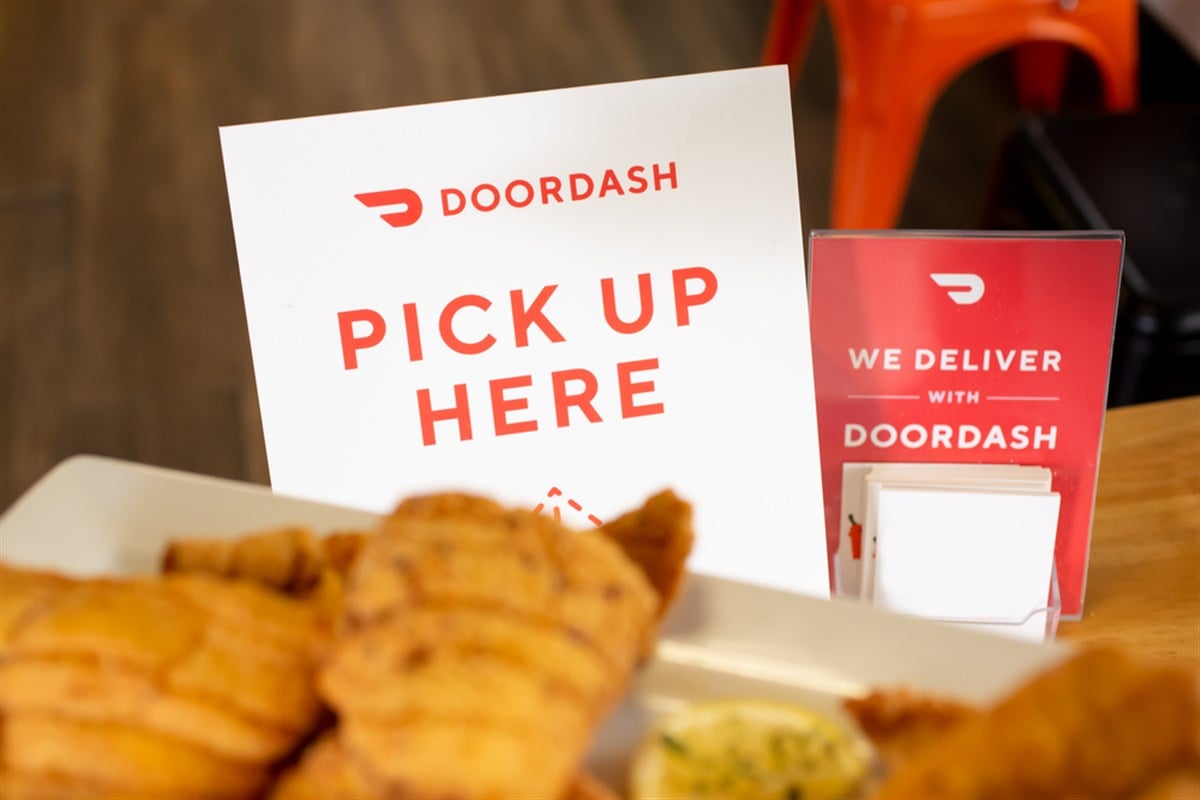 A view of a DoorDash pick up here sign on a table, and food in the foreground