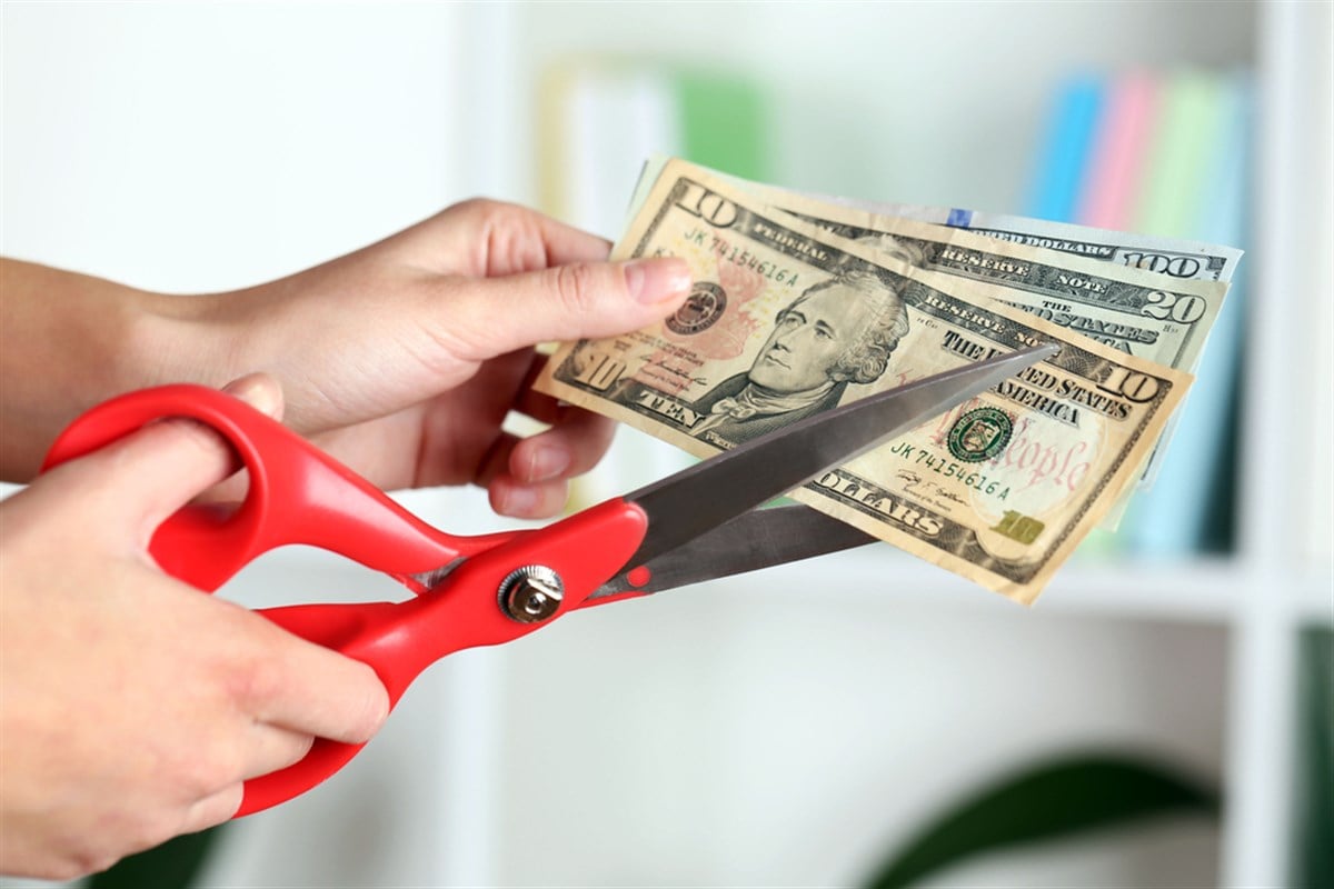 Hands with scissors cutting dollar banknotes, on blurred interior background