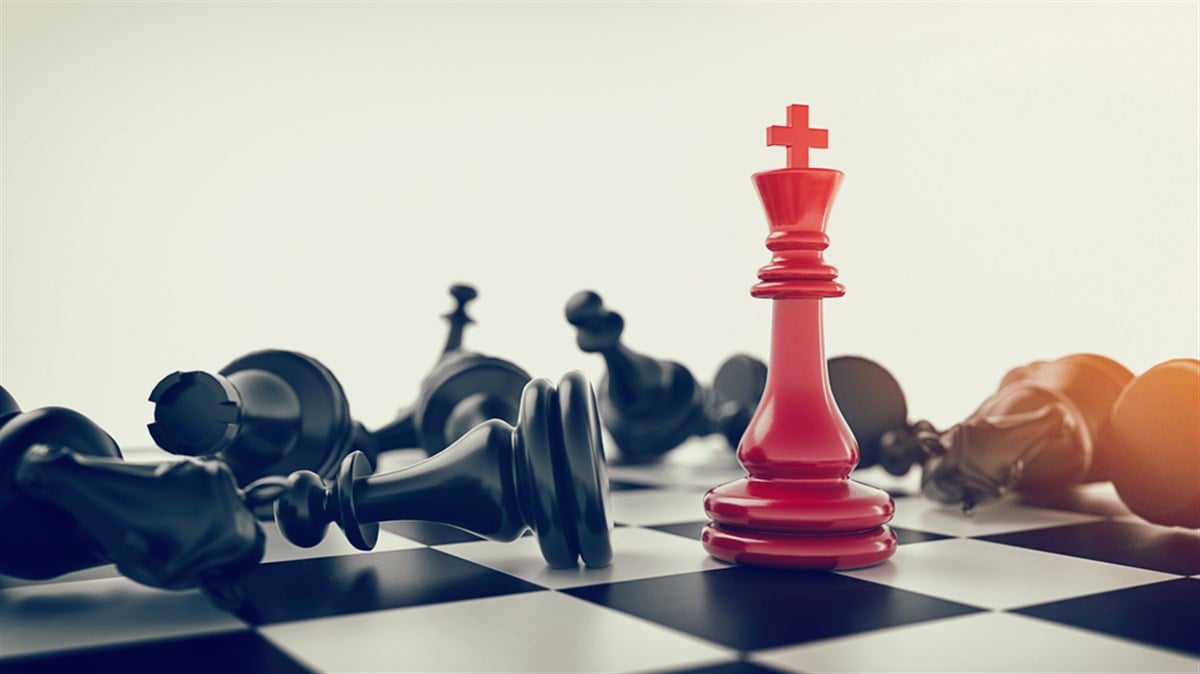 Photo of a red king chess piece surrounded by fallen black chess pieces.