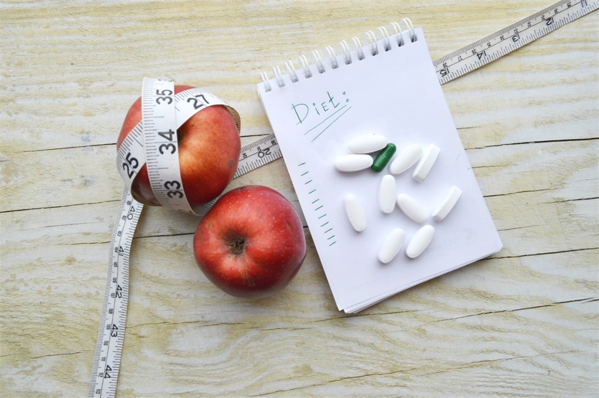 Two apples, measuring tape, pills and notebook - stock image