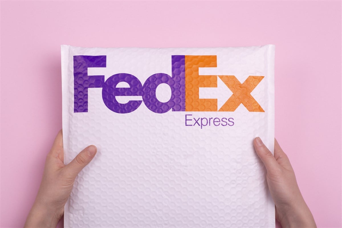 Delivery of parcels and cargo by FedEx Express. Hands delivering an order against a pink background.