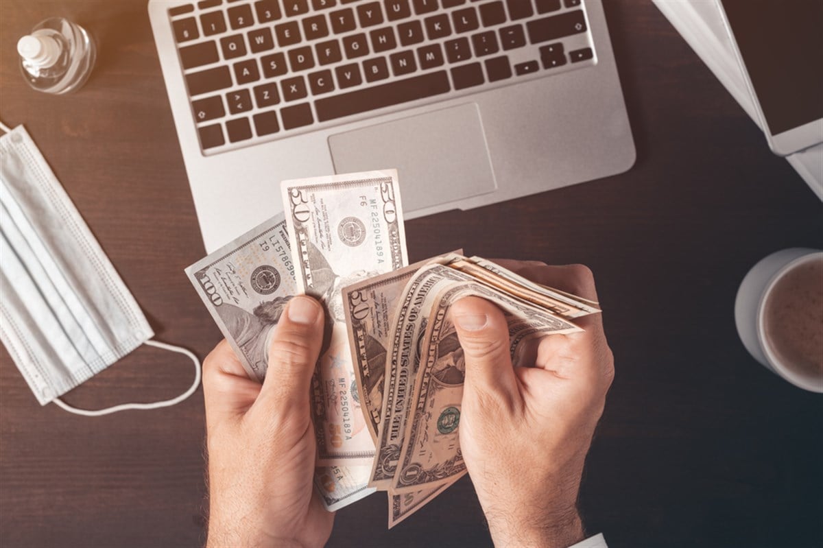 Businessman counting american dollar paper currency cash at office desk, top view of male hands with money