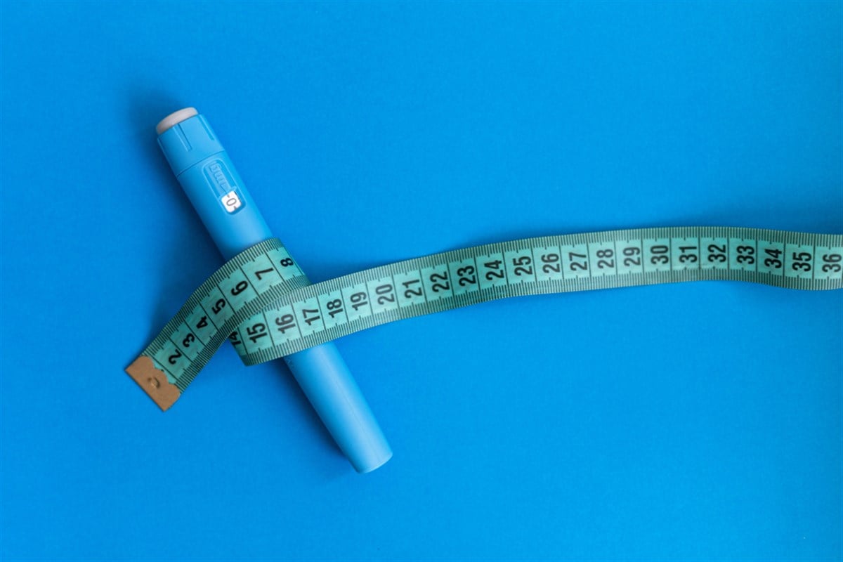 Blue injector dosing pen for subcutaneous injection of antidiabetic medication, anti-obesity medication on a blue background. Measuring tape around the injector. Drug and weight loss — Photo