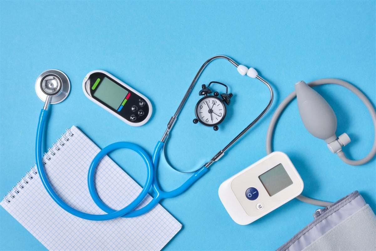 Digital blood pressure monitor, glucometer, stethoscope, notepad and alarm clock on blue background top view — Photo