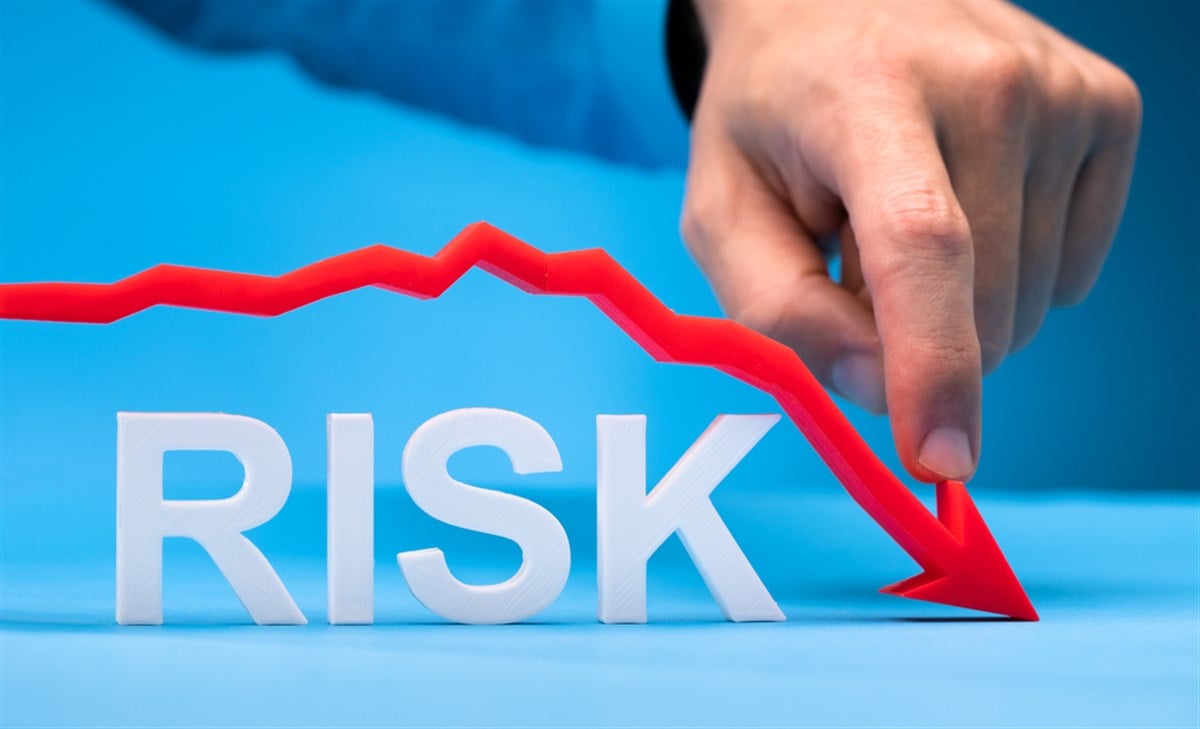 Photo of a finger pushing down a red chart arrow above the word RISK