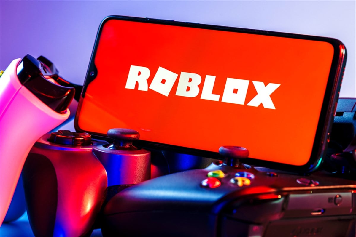 Kazan, Russia - August 25, 2021: Roblox is an online game platform and game creation system. A smartphone with the Roblox logo on the screen on the pile of the gamepads. - Stock Editorial Photography