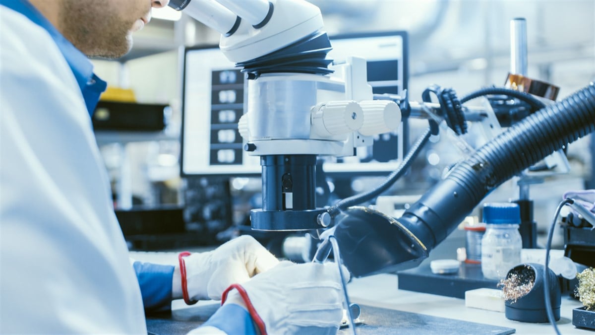 Close-Up Photo of an Electronics Factory Worker in White Work Coat Soldering a Printed Circuit Board Through a Digital Microscope