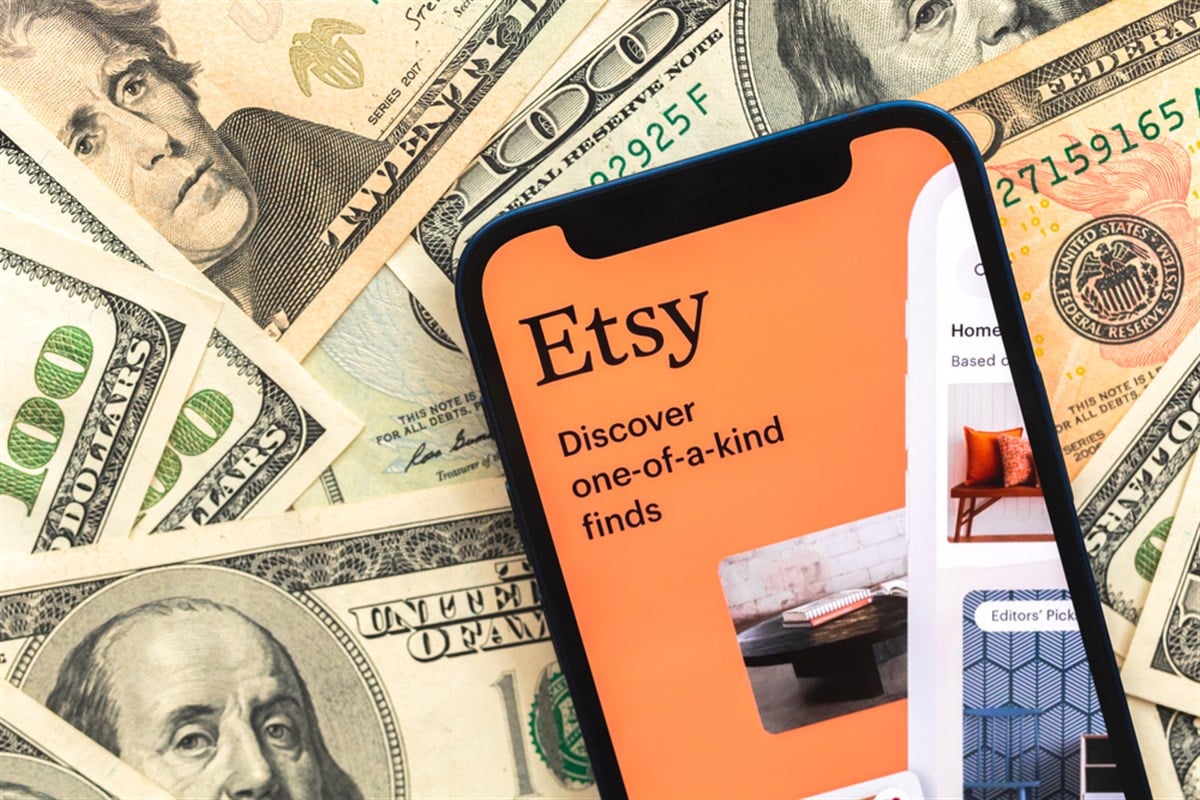 Poltava, Ukraine - April 28, 2022: Etsy shopping app logo on mobile phone screen. Business background with dollar money banknotes — Stock Editorial Photography