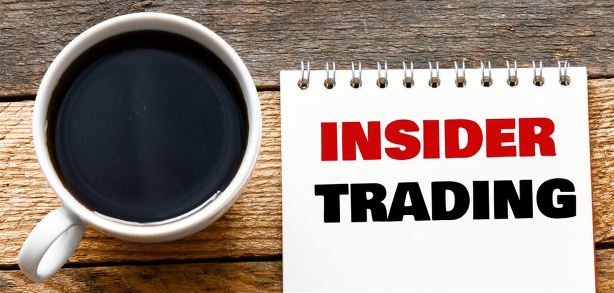 INSIDER TRADING words in a notebook on a wooden desk.