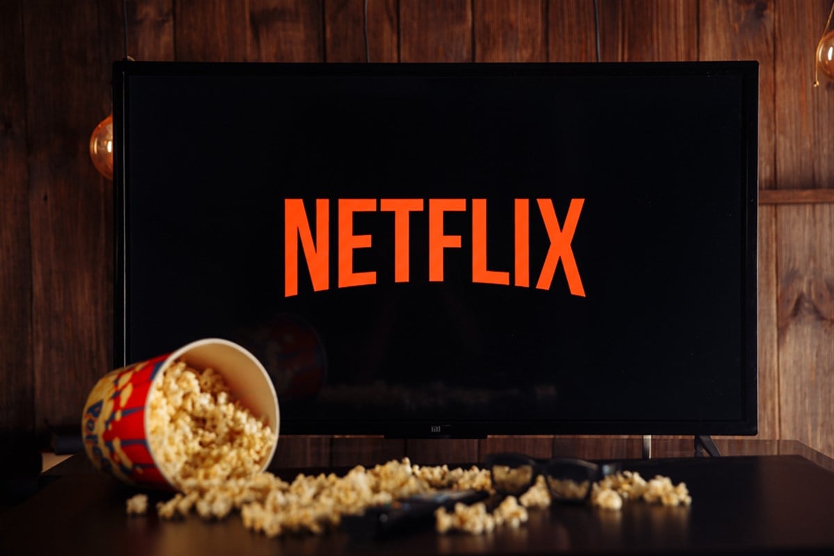 Photo of a Netflix logo on a TV screen, a container of spilled popcorn across the table in front of it.