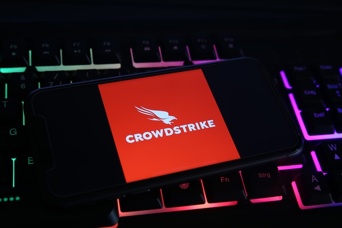 Closeup of mobile phone screen with logo lettering of crowdstrike cyber security company on computer keyboard (focus on upper part of bird logo)