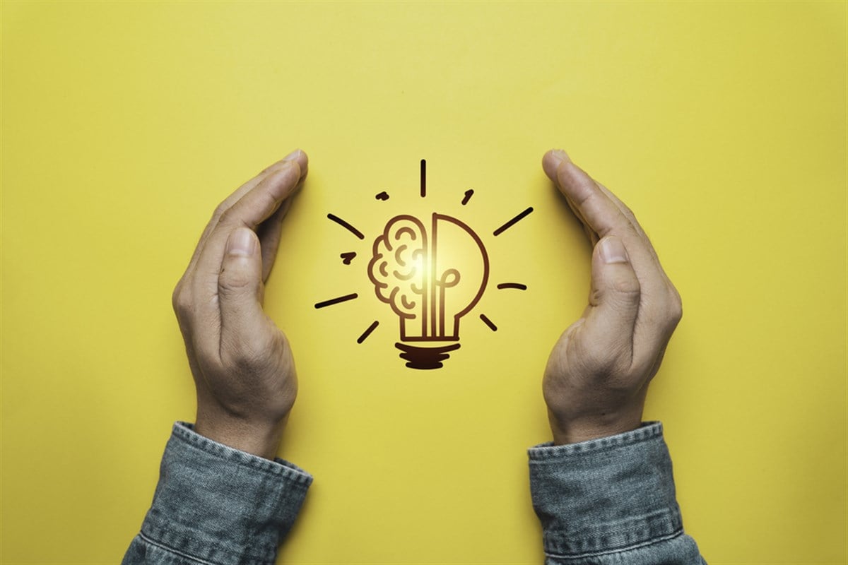 Photo of two hands cupping a glowing lightbulb on yellow background