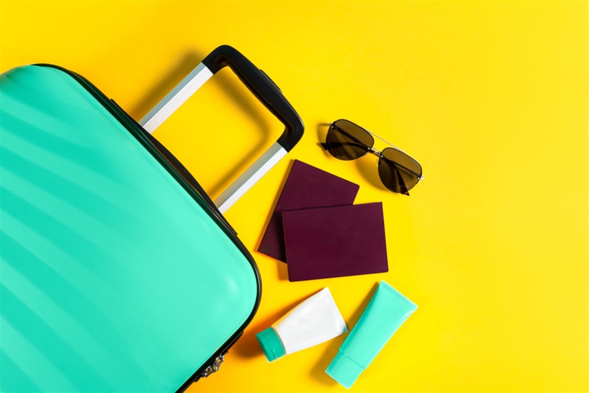 Bright and stylish cabin size suitcase with straw hat, sunscreen and passports - stock image