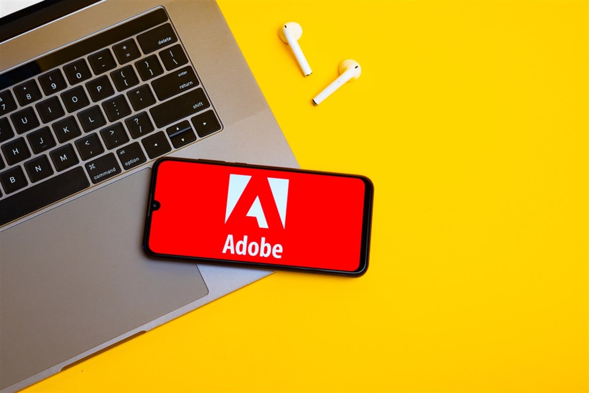 Kyoto city, Japan - July 31, 2023: Adobe logo on the smartphone screen is placed on the Apple macbook keyboard on yellow desk background. — Stock Editorial Photography