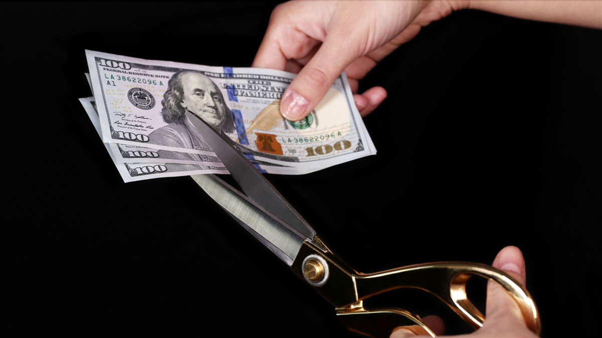 Hands with scissors cutting dollar - stock image