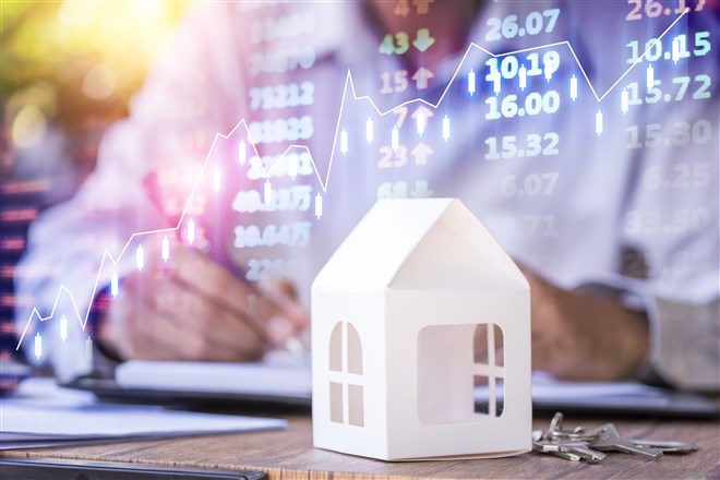 closeup of model house with man and stock market chart in background