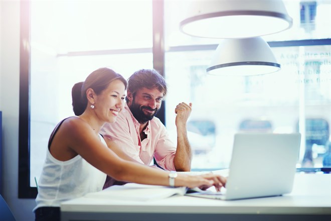 Couple of young office professionals talking over a laptop, using monday.com