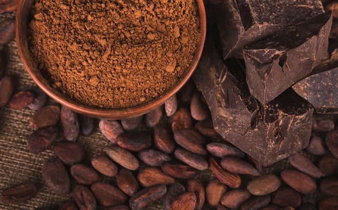 Raw cocoa beans, clay bowl with cocoa powder, black chocolate on brown sacking, top view