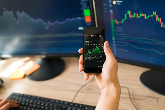 Rear view of a young man holding his smartphone while investing and checking the rise of the stock market