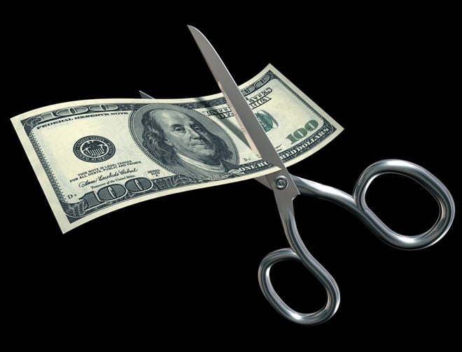 Conceptual photo of a dividend cut - a pair of scissors cutting through a $100 bill on a black background.