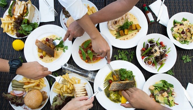 Photo of Various types of food laid out on a table with people digging in with forks. Representative of index funds being able to try every stock on the menu.