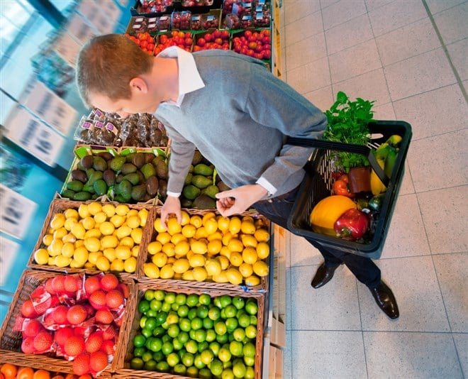 Photo of man in grocery store picking fruit to put in a basket that contains a variety of fruit. Representative of a basket of stocks, like mutal or index funds.
