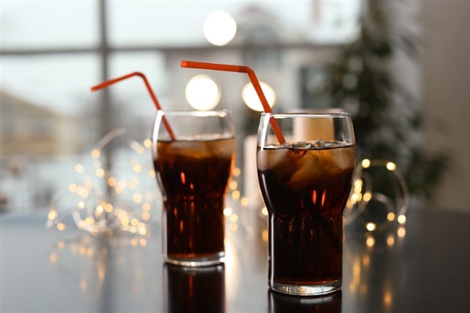 Glasses of cold cola and fairy lights on table - stock image