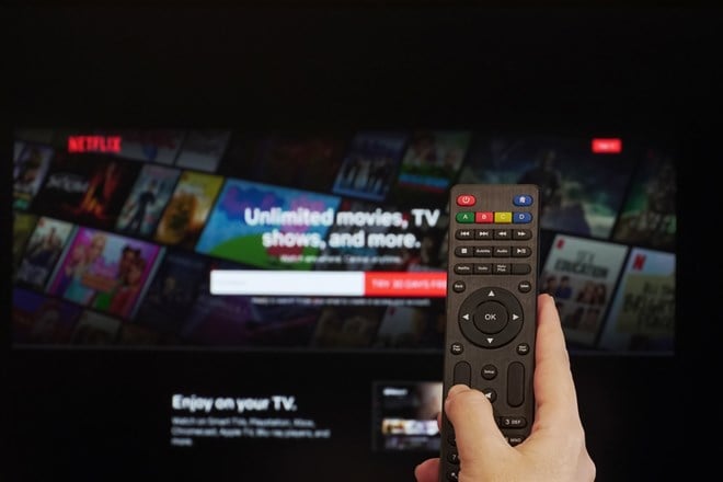 Netflix streaming Service Hand holds a remote control before a screen with Netflix app online watch login page