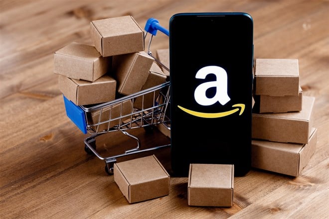 Smartphone with Amazon logo on the screen, shopping cart and parcels. 