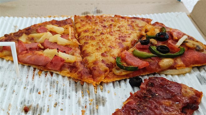 Sliced pizza garnished with cheese, ham, sausage and bell pepper