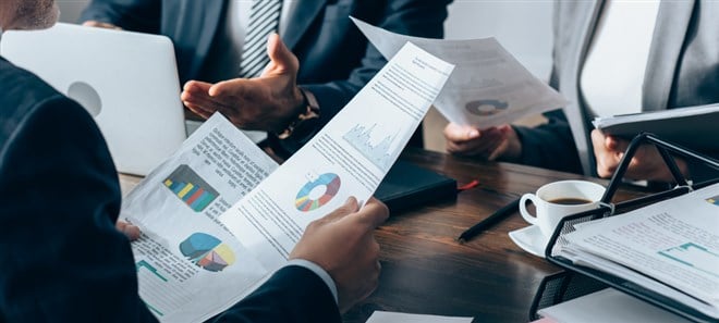 Cropped view of advisor holding papers with charts near business people, laptop and notebook on table, banner